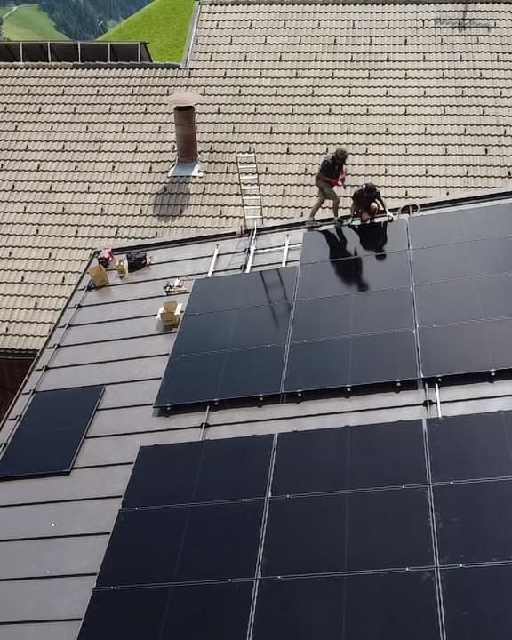 Zwei ELMETIC-Monteure verlegen Photovoltaik-Module auf dem Dach eines Bauernhauses in Osttirol